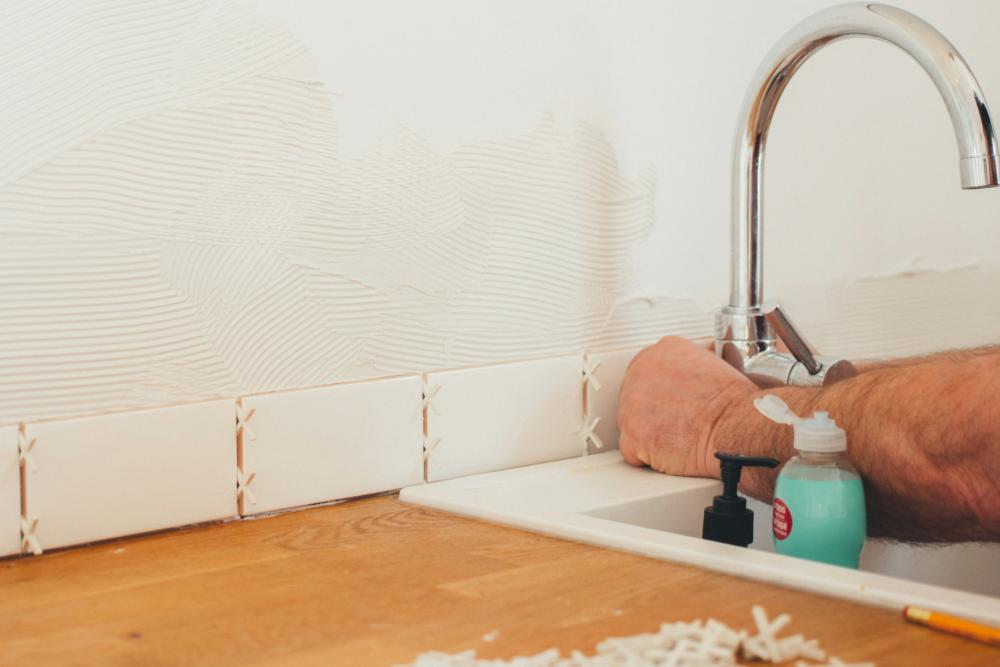 Weiße Wand, Waschbecken mit silberner Armatur, die von Person repariert wird, Mita-On GmbH