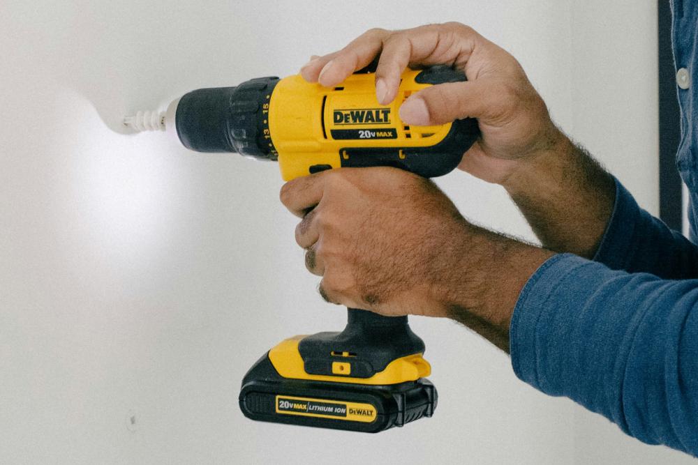 Person hält gelbe Bohrmaschine "DeWalt" vor einer Wand, Mita-On GmbH