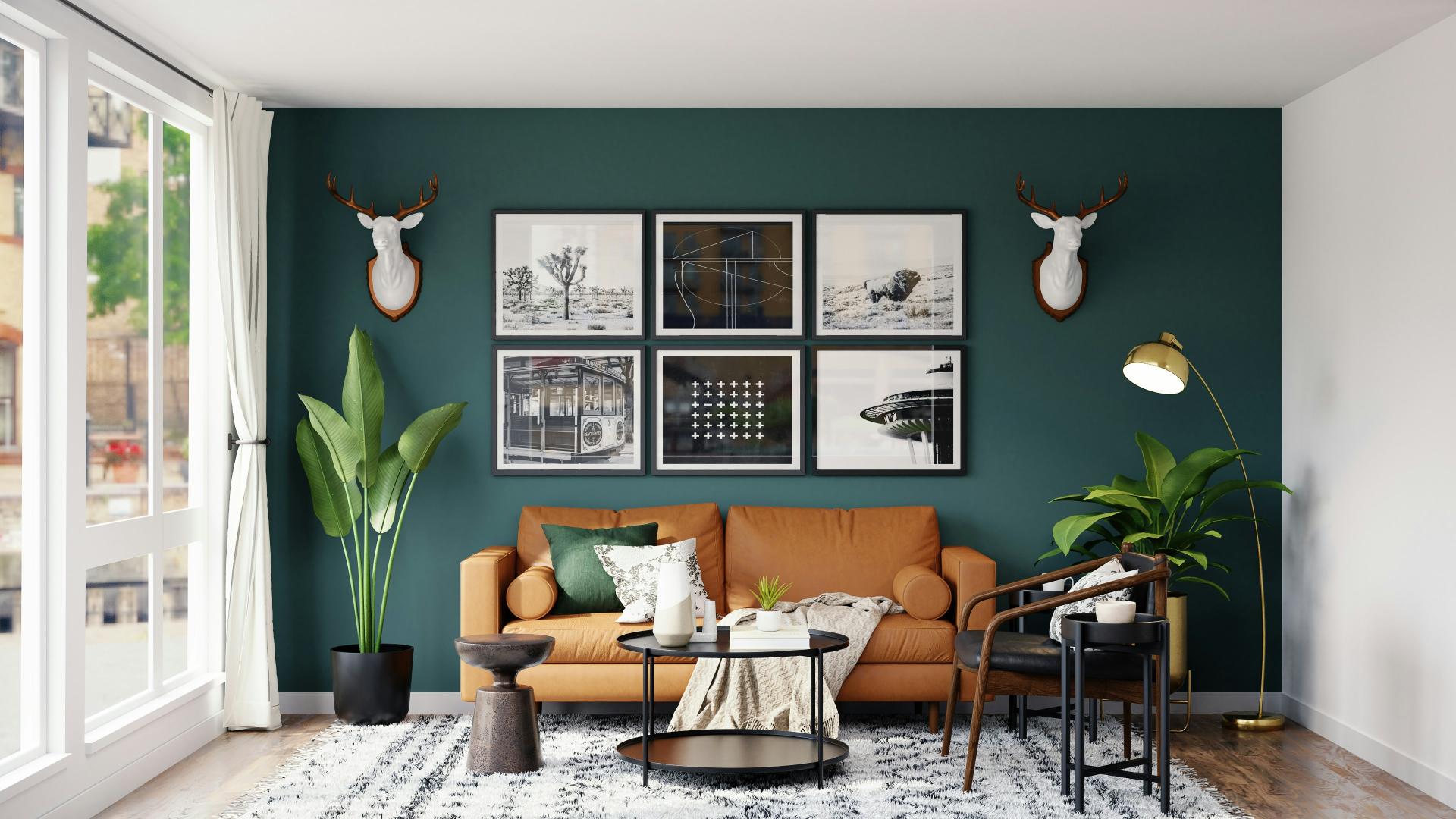Hellbraunes Ledersofa vor dunkelgrüner Wand mit sechs Bildern, zwei Keramik-Hirschgeweihen, Grünpflanzen, schwarzer Couchtisch und goldene Stehlampe, Mita-On GmbH